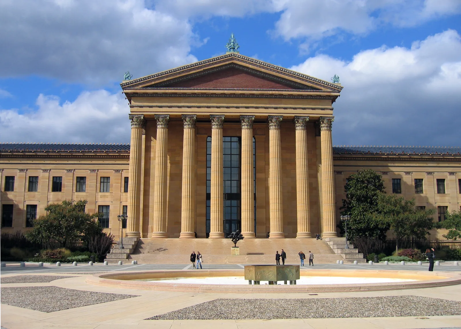 Fachada de un museo de estilo neogriego con altas columnas bajo un cielo azul con nubes